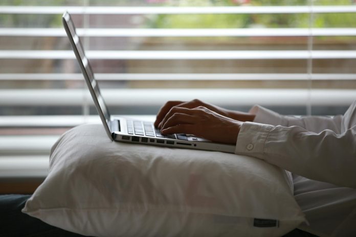 person wearing white dress shirt using silver laptop on top of white throw pillow